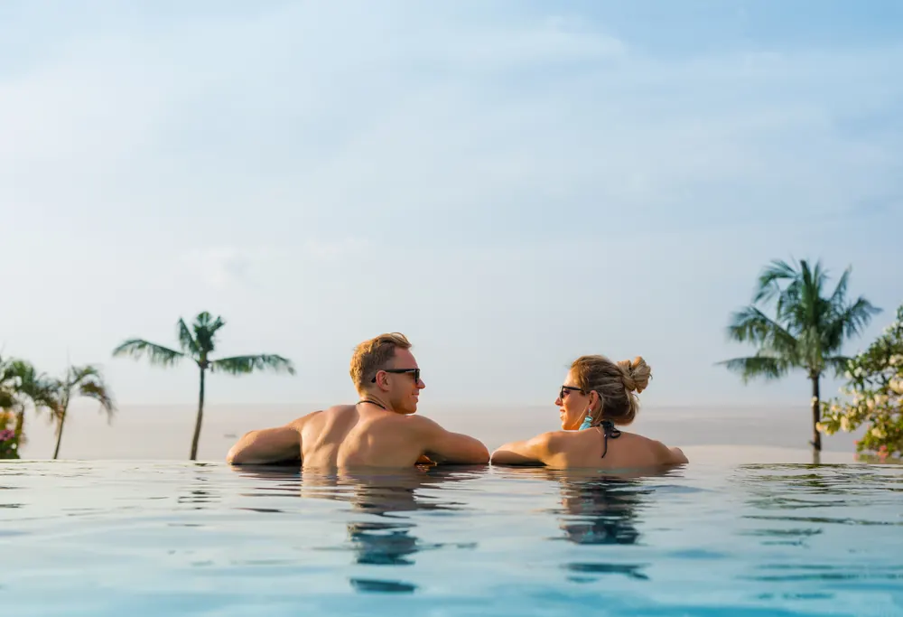 Couple relaxing together in an infinity pool with palm trees and open water